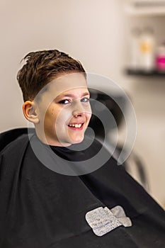 Little kid covered with black cloth by hairdresser