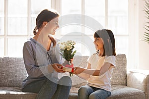 Little kid daughter giving mom receiving gift box and flowers