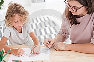 Little kid drawing a house using colorful crayons with his female, therapist during a meeting in the office photo