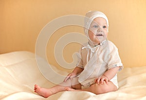 Little kid dressed in white sits on the bed smilin