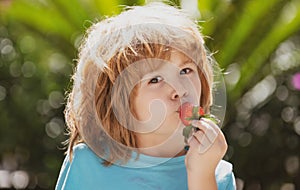 Little kid eating strawberry in nature. Child enjoys a delicious berry on green summer background. Close up kids happy