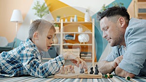 Little kid enjoying chess game with caring father spending leisure time at home