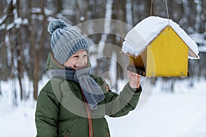Little kid feeding birds in winter in the forest.
