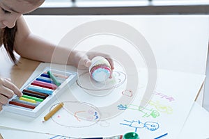 Little kid girl choosing crayon color to decorate Easter egg in hand. Cute child prepare for Easter holiday at home