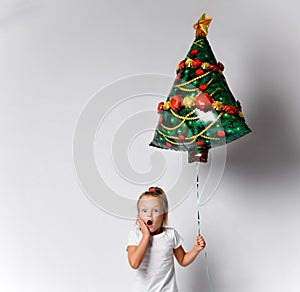 Little kid girl with christmas tree air balloon is awing, surprised, excited on white background with free copy space.