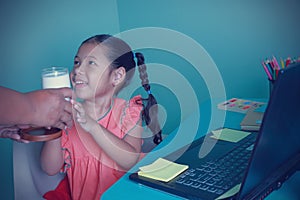 Little kid girl cute get a glass of milk from a mom before studying distance education. During the coronavirus outbreak, the