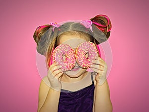 A little kid girl dabbles and plays with two fresh donuts before eating. A child holds donuts near his eyes and looks through the