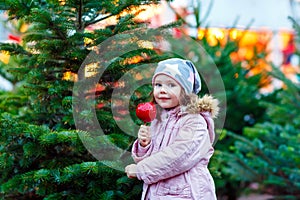 Little kid girl eating crystalized apple on Christmas market