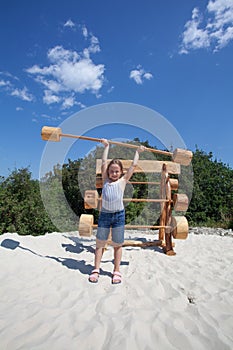 Little kid girl holding barbell up on summer playground. Happy childhood and girls power concept