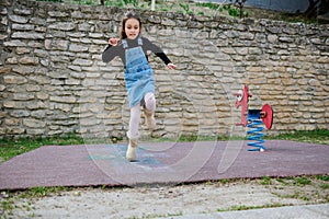 A little kid girl jumping on one leg, playing hopscotch on an urban playground outdoors. Hopscotch popular street game