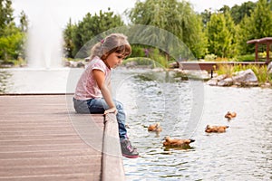 Little kid girl is melancholy sitting on pier