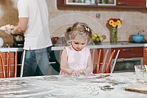 Little kid girl play with flour while daddy cooking in kitchen at table. Happy family dad, child daughter cooking food