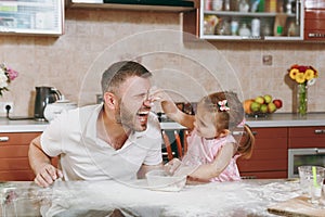 Little kid girl play with man smearing dad with flour in kitchen at table. Happy family dad, child daughter cooking food