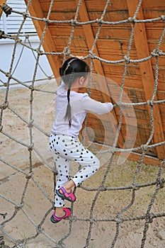 Little kid girl at playground playing on climbing rope net