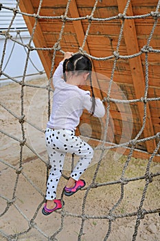 Little kid girl at playground playing on climbing rope net