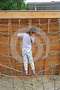 Little kid girl at playground playing on climbing rope net