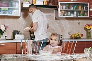 Little kid girl plays with flour while daddy cooking in kitchen at table. Happy family dad, child daughter cooking food