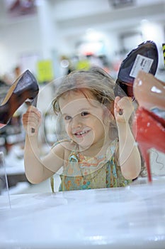 Little kid girl in a shoes store with the shoes on a shop-window.