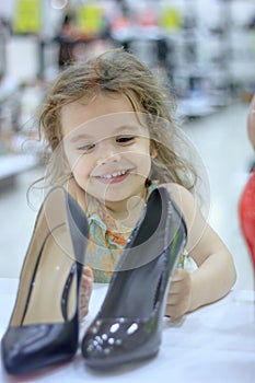 Little kid girl in a shoes store with the shoes on a shop-window.