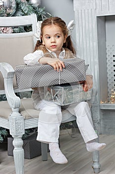 Little kid girl sitting in chair with christmas gift box.