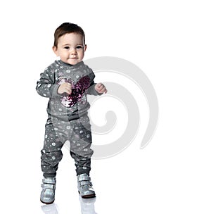 Little kid in gray suit with snowflakes print and boots. She is smiling, stomping on floor, isolated on white background. Close up