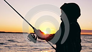 Little kid is handling a fishing pole while angling at sunset