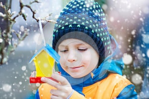 Little kid hanging bird house on tree for feeding in winter