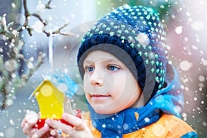 Little kid hanging bird house on tree for feeding in winter