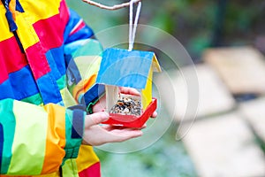 Little kid hanging bird house on tree for feeding in winter