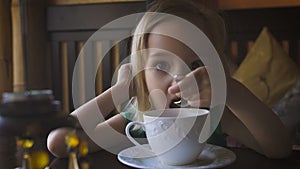 A little kid having breakfast at a cozy cafe. An adorable girl drinking tea and enjoying her breakfast.