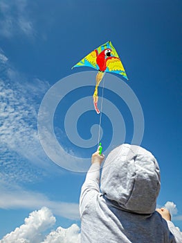 little kid in a hood plays a kite on the seashore