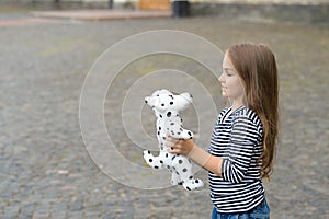 Little kid with long hair in casual fashion style play with toy dog outdoors, shop, copy space
