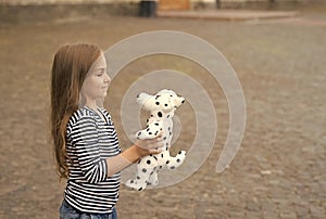 Little kid with long hair in casual fashion style play with toy dog outdoors, shop, copy space