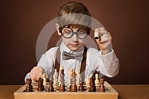 Little Kid playing Chess Game. Intelligent Small Boy in Eyeglasses next to Chessboard. Child Education and Development