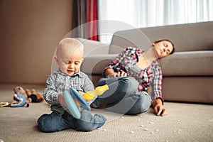 Little kid playing on the floor, mother sleeps