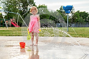 Little kid playing at water splash pad in the park playground during hot summer day