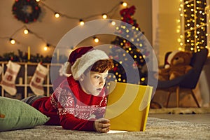 Little kid reading a book of wonderful stories and fairy tales on Christmas Eve at home