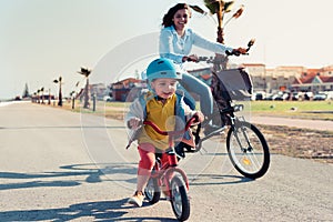 Little kid riding a balance bike with his mother on a bicycle