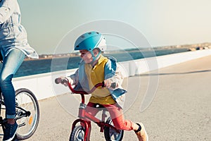 Little kid riding a balance bike with his mother on a bicycle