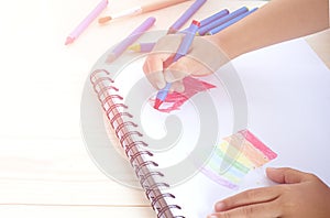 Little kid`s hand drawing red heart on white paper.