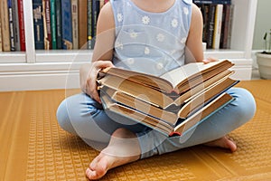 Little kid sitting in the front of bookshelf and holds few books in the hands. Concept of education
