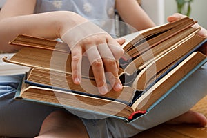 Little kid sitting in the front of bookshelf and holds few books in the hands. Concept of education