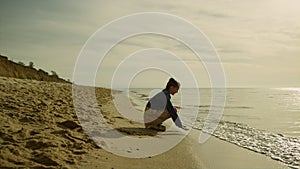 Little kid touching sea waves on sunset beach. Cute girl playing sand at ocean.