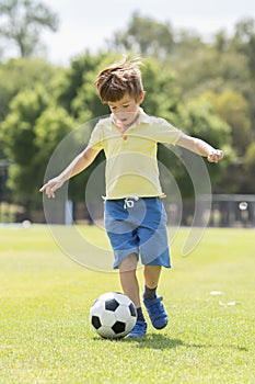 Little kid 7 or 8 years old enjoying happy playing football soccer at grass city park field running and kicking the ball excited i