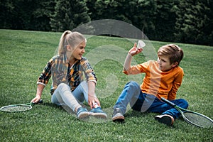 Little kids with badminton rackets and shuttlecock sitting on the grass at park