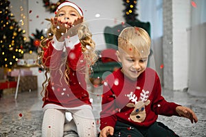 Little kids in christmas costume having fun beside a decorated christmas tree.