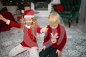 Little kids in christmas costume having fun beside a decorated christmas tree.