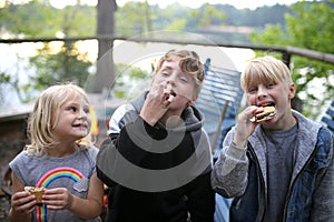 Little Kids Eating Smore`s with Marshmallows by Fire While Camping on Lake