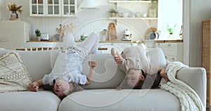 Little kids fooling around lying upside down on cozy sofa