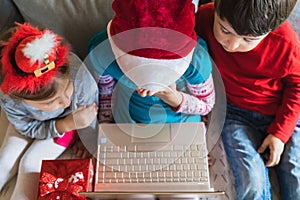 Little kids girls, boy have video call, onine virtual conference in laptop.Red Christmas santa claus,elf hat. Congratulations,